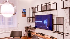 Une chambre moderne dotée d’un grand téléviseur à écran plat, d’un bureau en bois, de deux chaises et d’une étagère décorative.