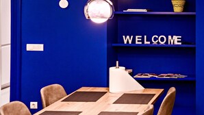 Une chambre moderne avec un mur bleu, une table en bois ornée d’un motif géométrique et une étagère sur laquelle est posé un panneau indiquant « BIENVENUE ».