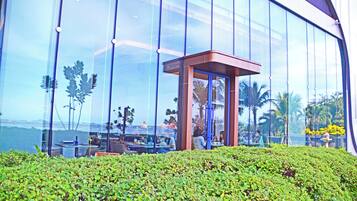 A modern building with large glass windows, a small enclosed area with a roof, and a well-maintained green hedge in the foreground.