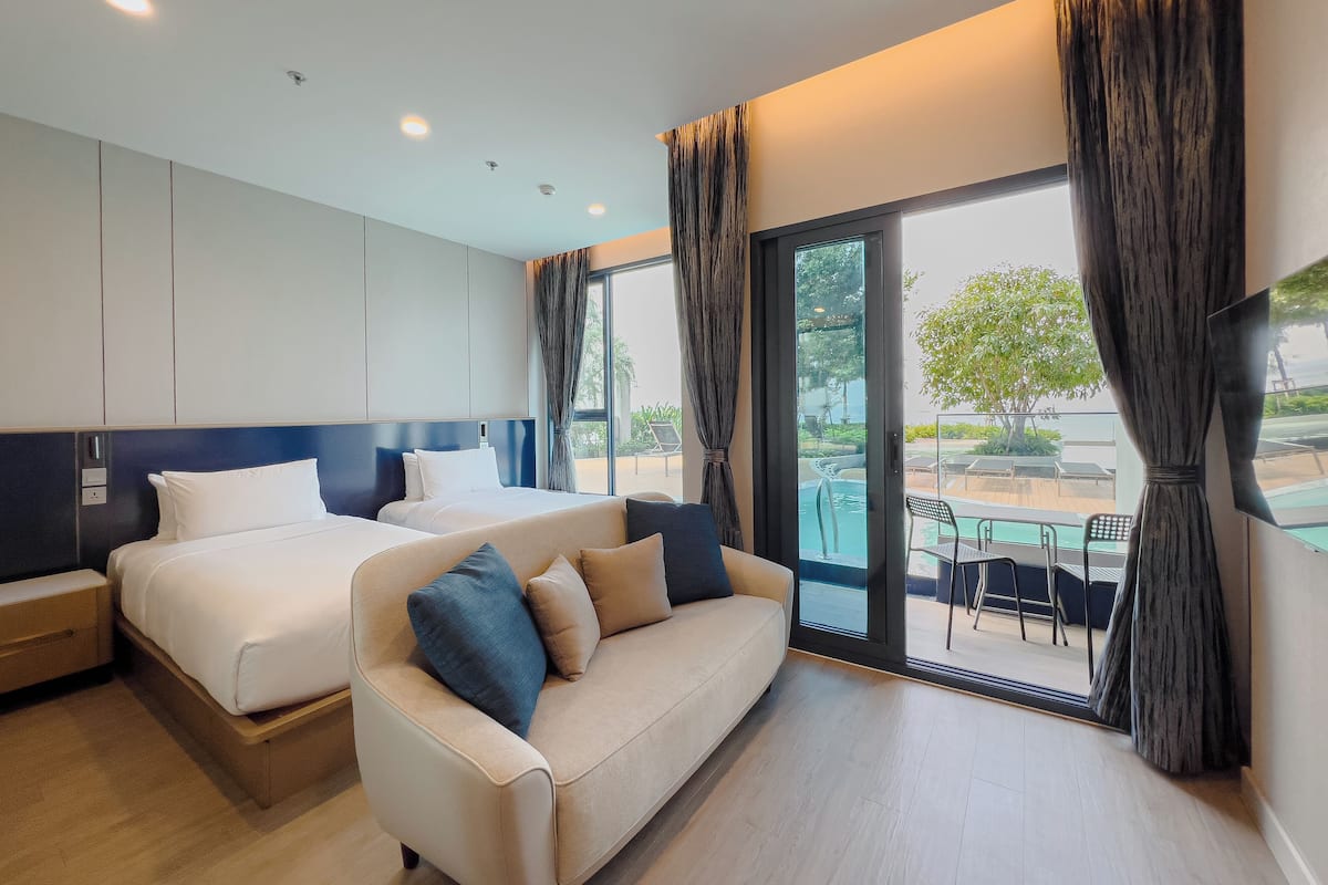 Ein modernes Hotelzimmer mit zwei Betten, einer Sitzecke und einem großen Fenster mit Blick auf einen Pool und Sitzmöglichkeiten im Freien.