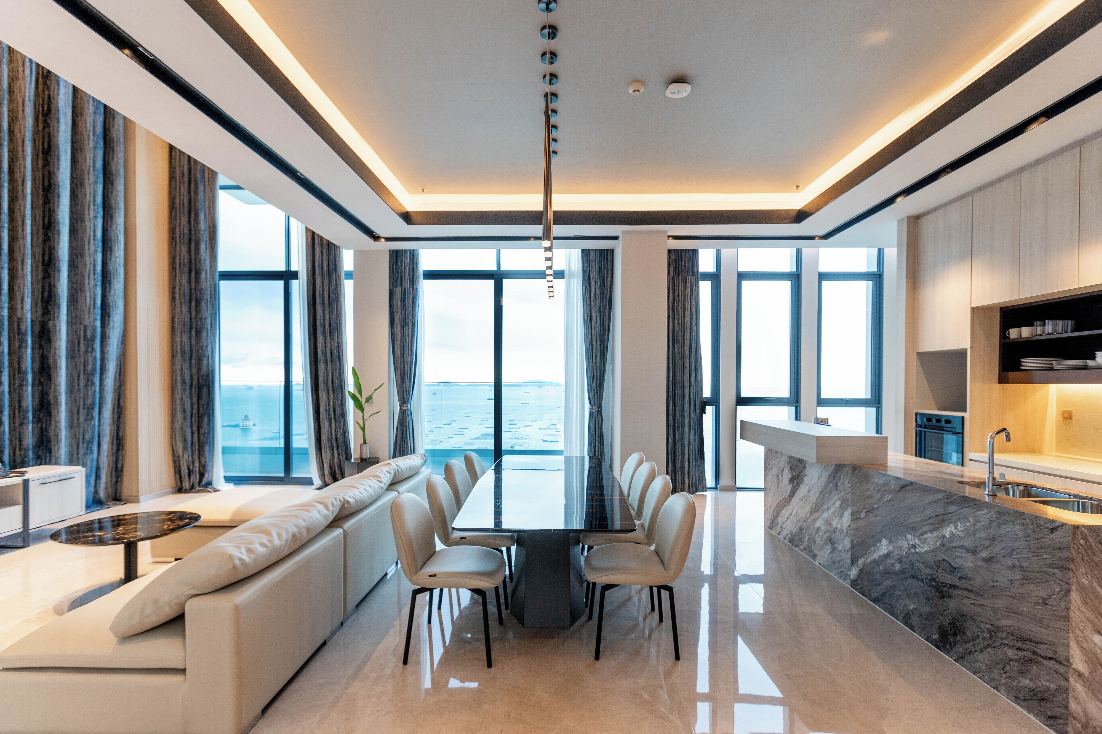 Una cocina moderna con encimera de mármol, zona de comedor con mesa de cristal y vistas al mar.