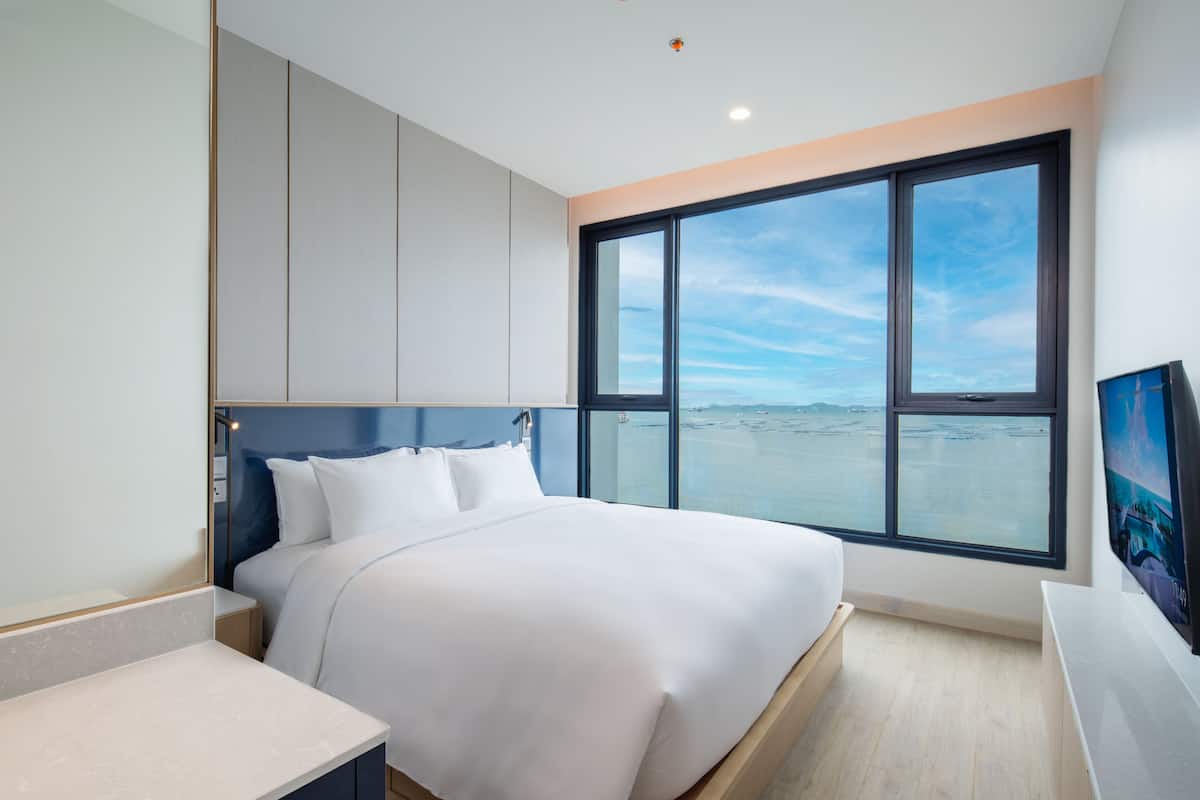 Ein modernes Hotelzimmer mit einem großen Bett, einem Schreibtisch und Meerblick durch ein großes Fenster.