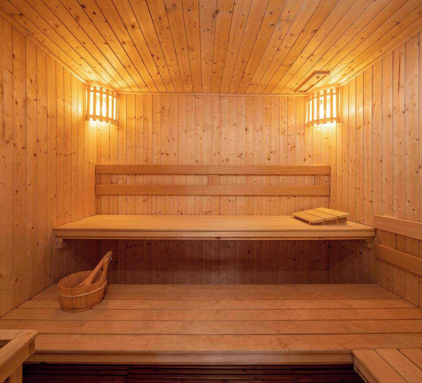A wooden sauna with benches and a bench seat, wooden walls, and two wall-mounted lights.