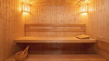 A wooden sauna with benches and a bench seat, wooden walls, and two wall-mounted lights.