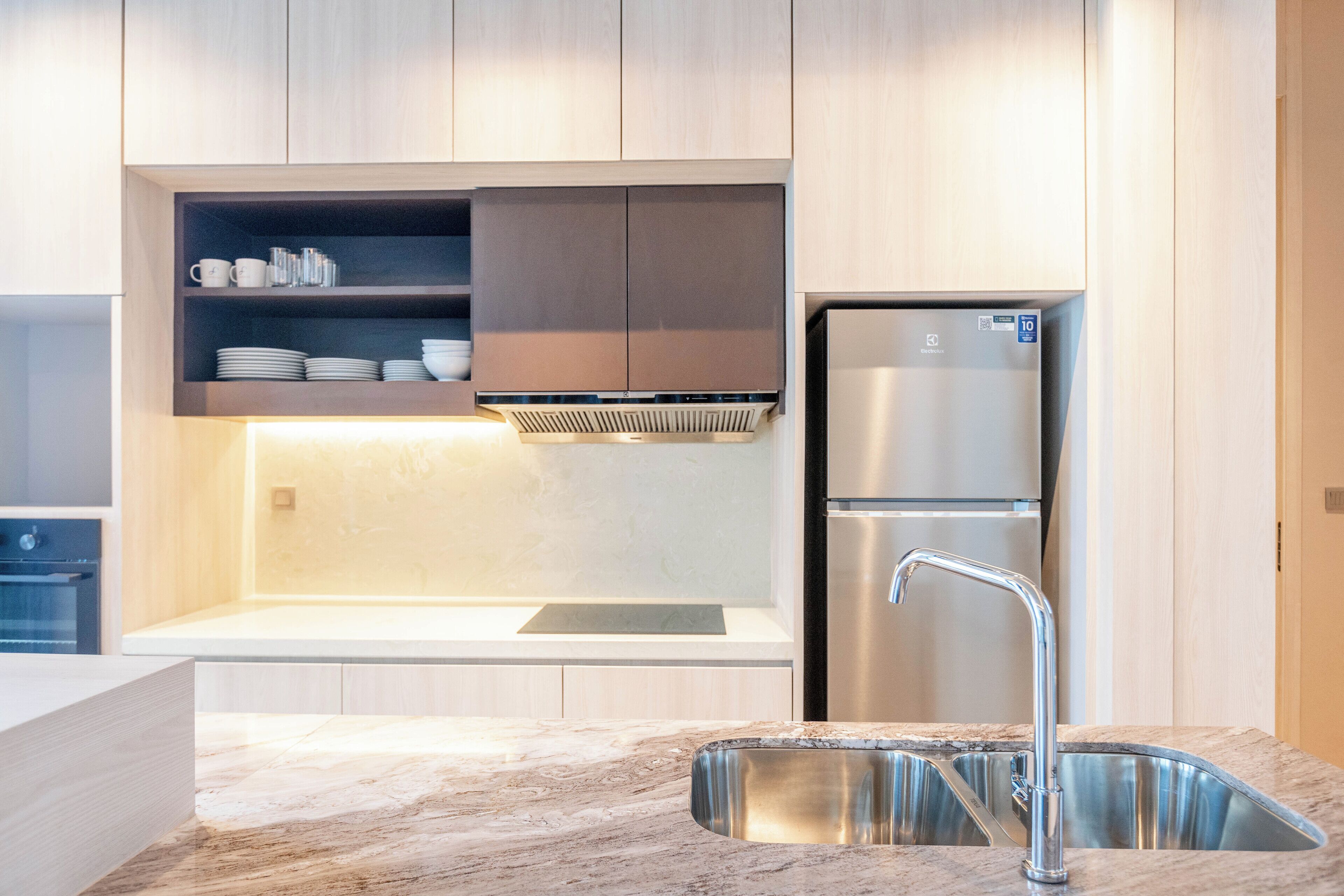 A modern kitchen with a stainless steel refrigerator, a built-in oven, and a marble countertop.