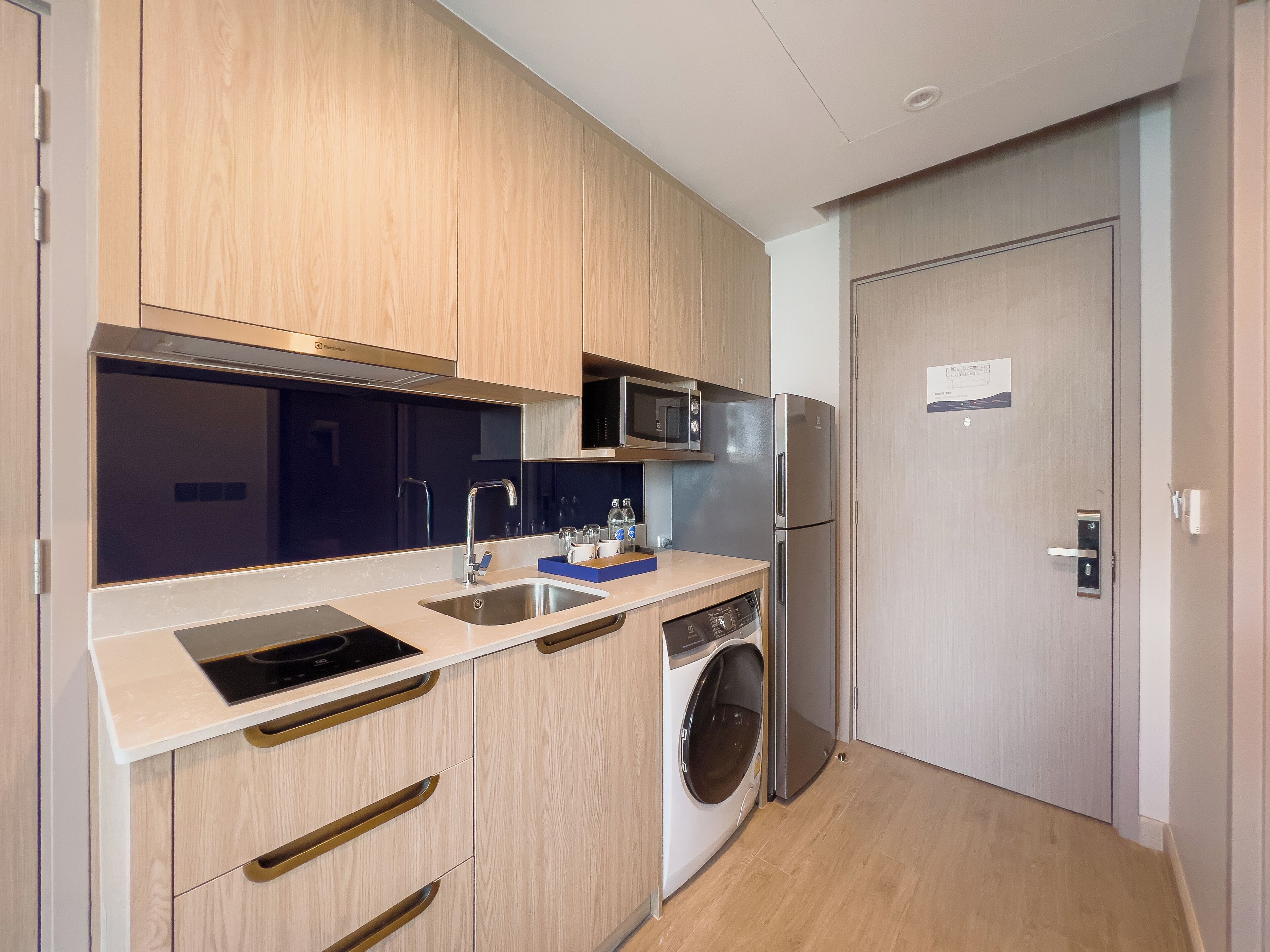 Une cuisine compacte dotée de meubles en bois, d’un évier en acier inoxydable, d’un four à micro-ondes, d’un réfrigérateur et d’un lave-linge encastré.