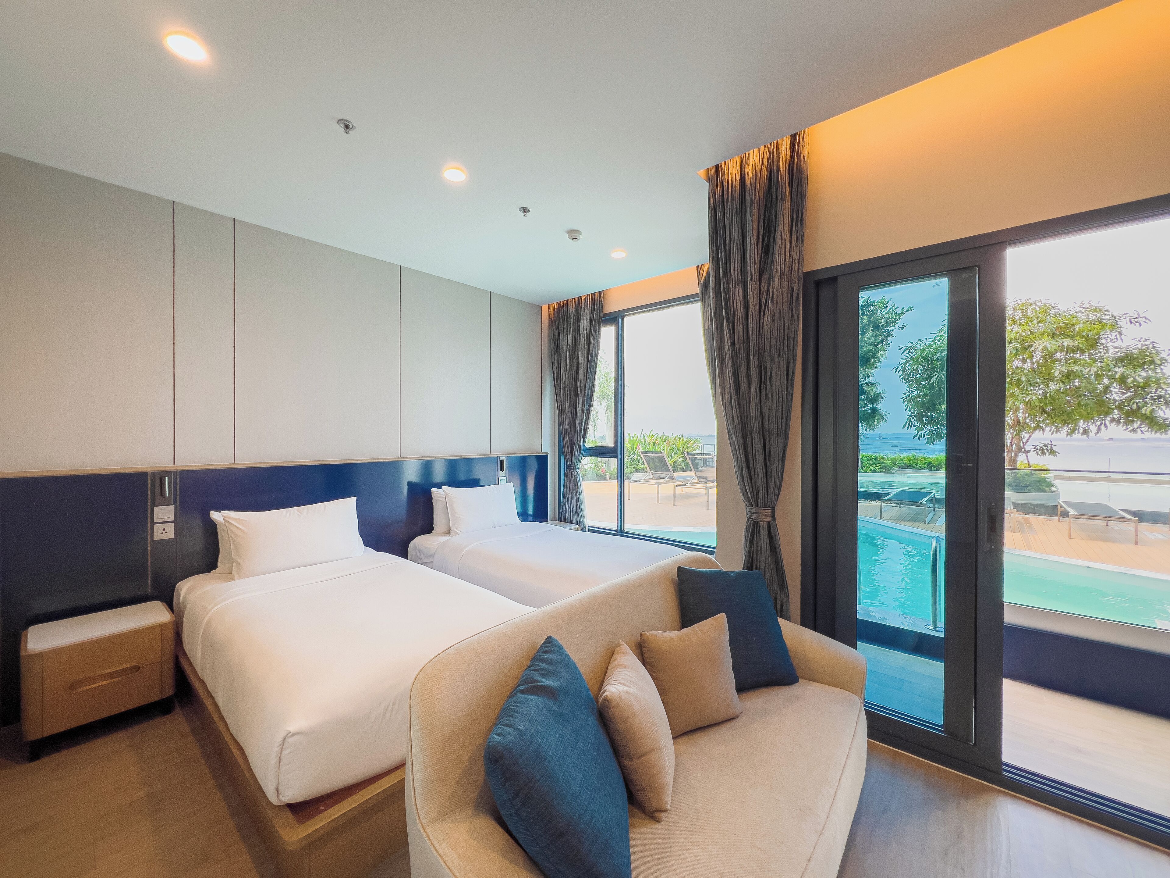 Habitación de hotel con dos camas, un sofá y un ventanal con vistas a una piscina y zona exterior.