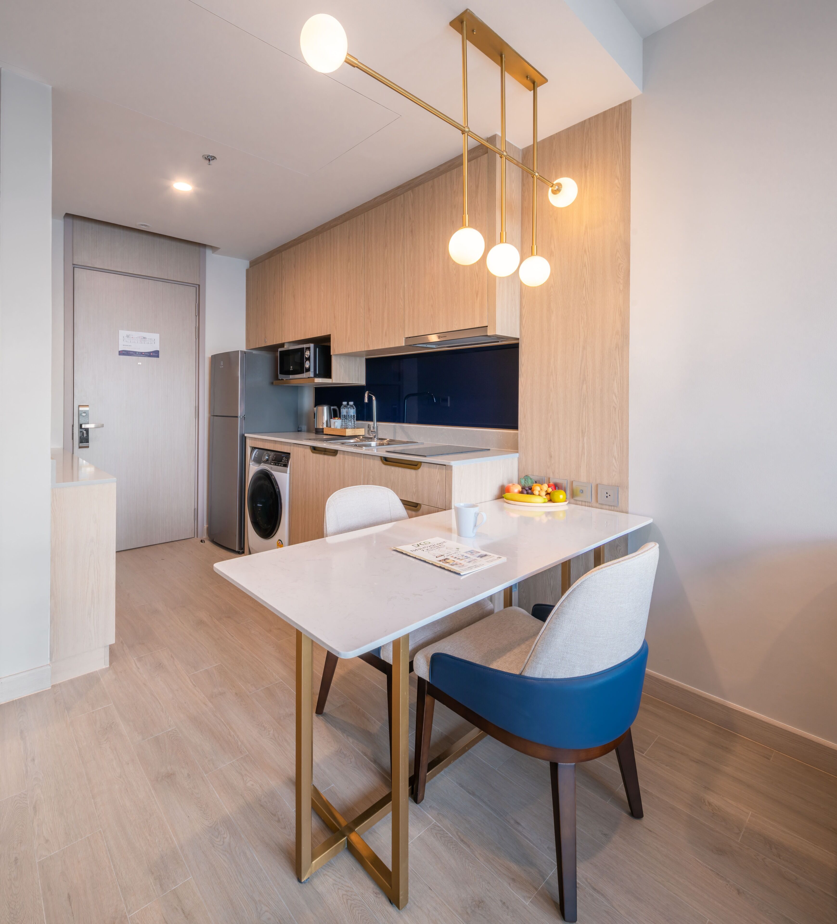Cocina moderna con microondas integrado, un lavamanos y una campana extractora de acero inoxidable. Hay una mesa de comedor con una silla y un frutero pequeño sobre la encimera.