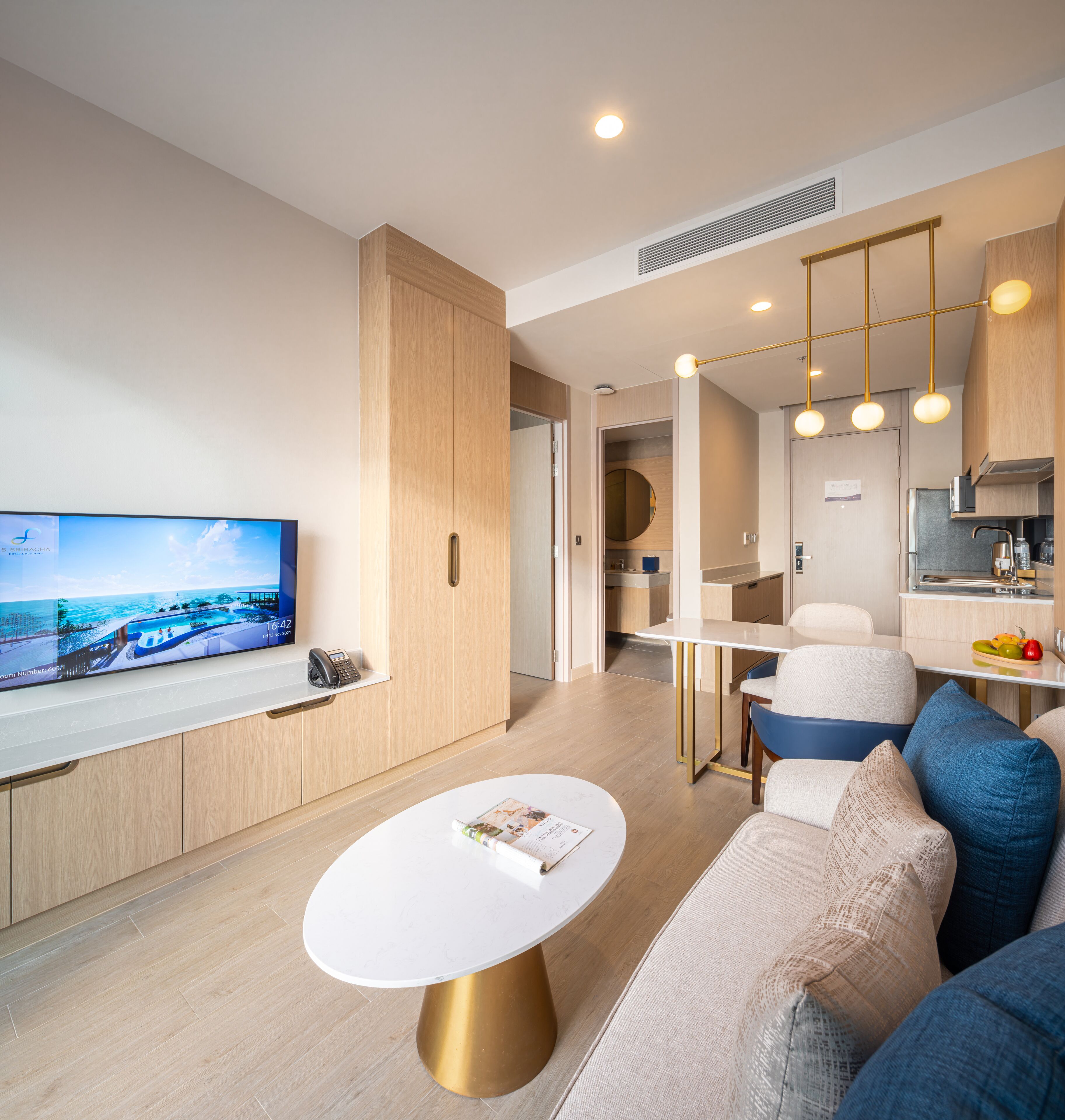 A modern living room with a flat-screen TV, a round coffee table, a sofa, and a kitchen area with a dining table.
