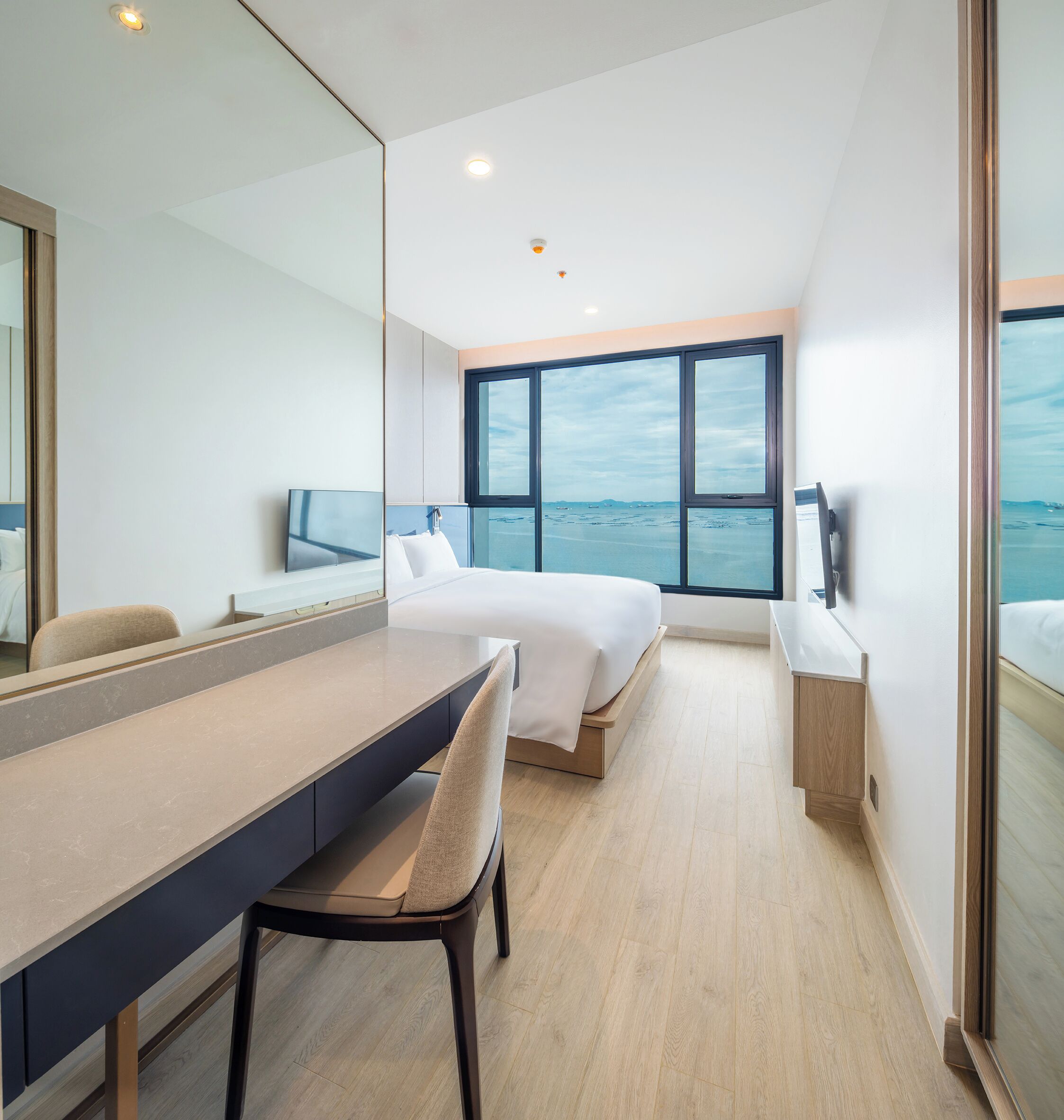 A modern hotel room with a large bed, a desk, and a TV.