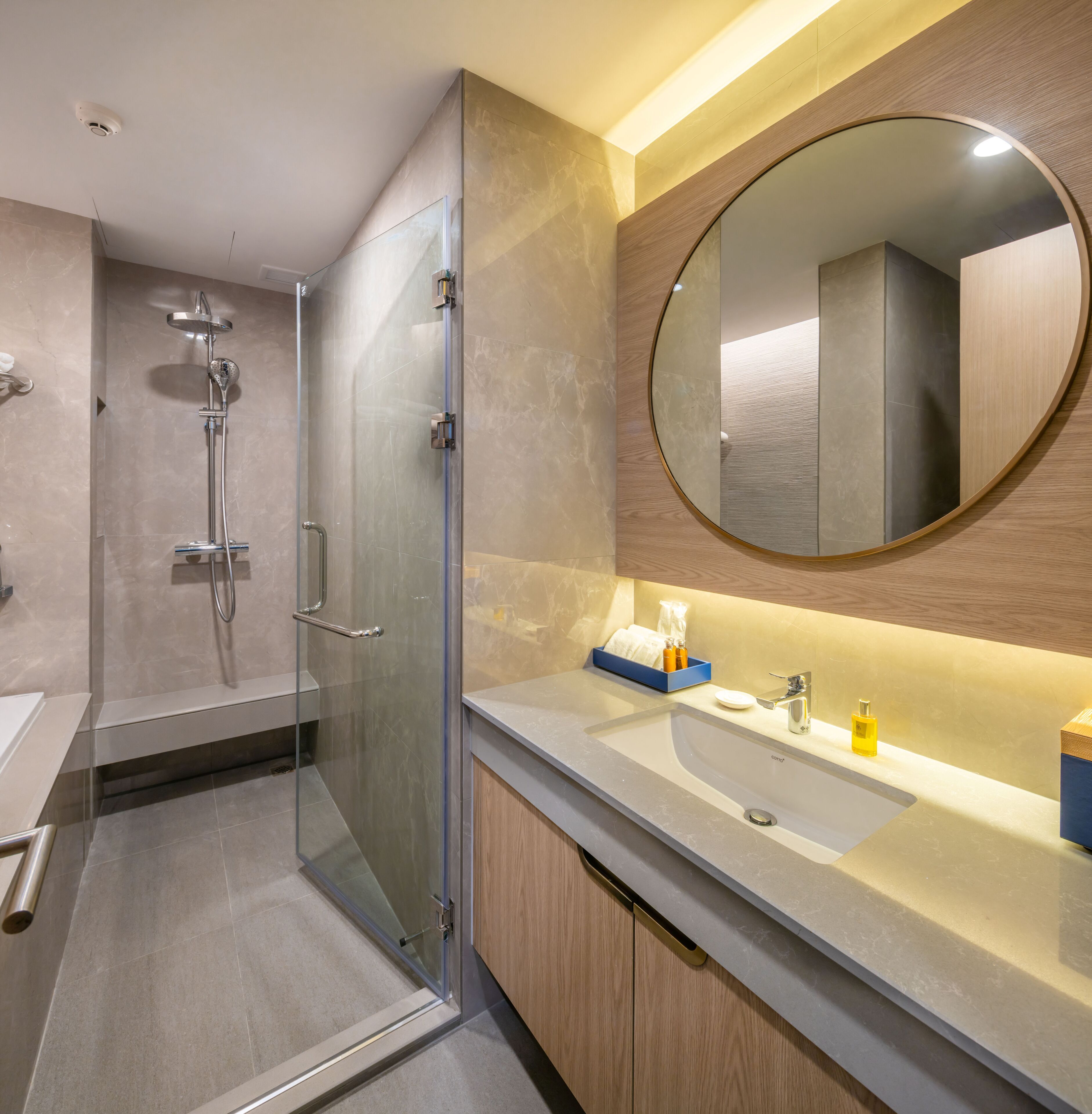 Un baño moderno con ducha de vidrio, un espejo grande y tocador con lavamanos y artículos de aseo.