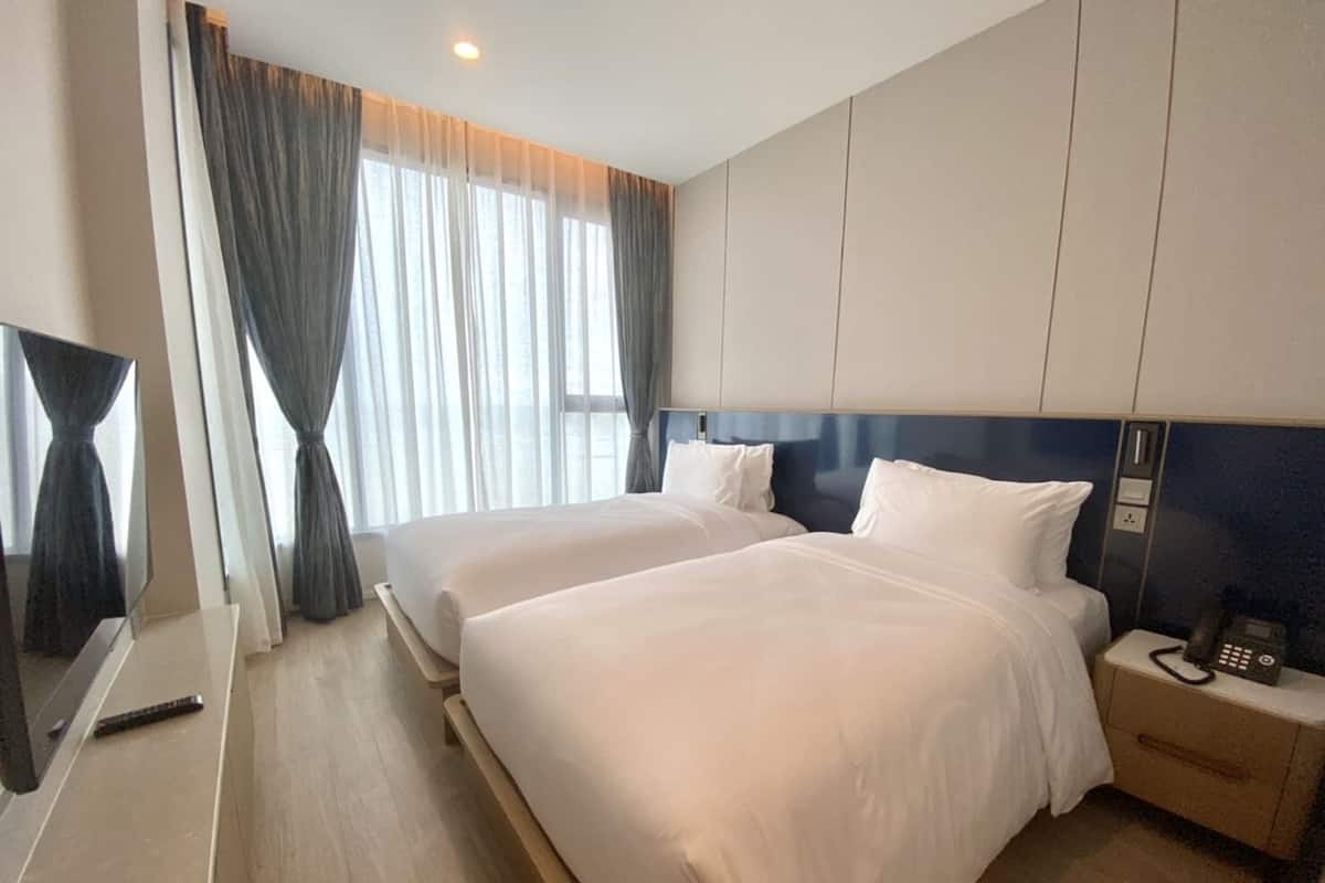 Ein Hotelzimmer mit zwei Betten, einem Fernseher, einem Nachttischtelefon und einem großen Fenster mit Vorhängen.
