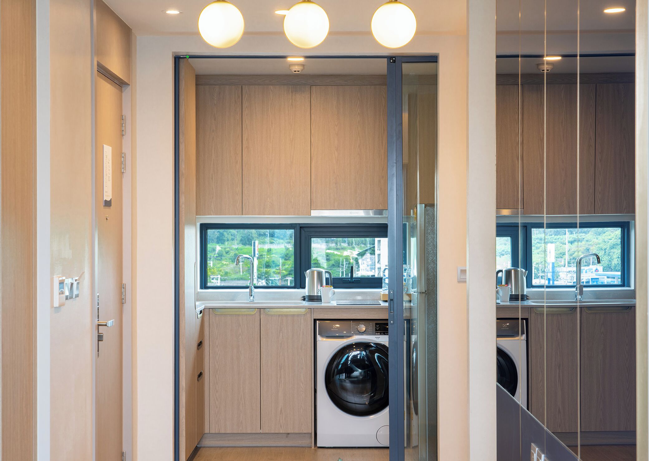 A compact kitchen with a built-in washer and dryer, wooden cabinets, and a window providing a view of greenery.