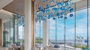 A modern lobby with a high ceiling, large windows, and a view of the sea.