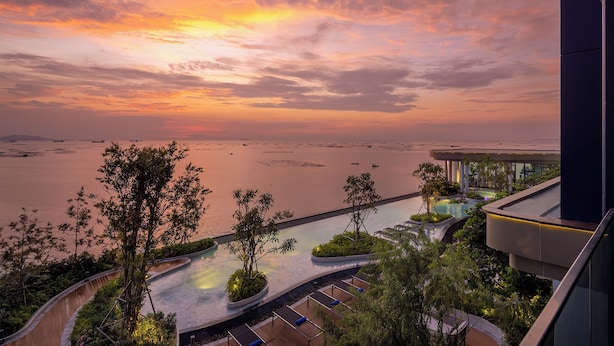 A resort with a pool, lush greenery, and a view of the water.