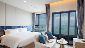A modern hotel room with a large bed, a sofa, a small table, and a view of the water.