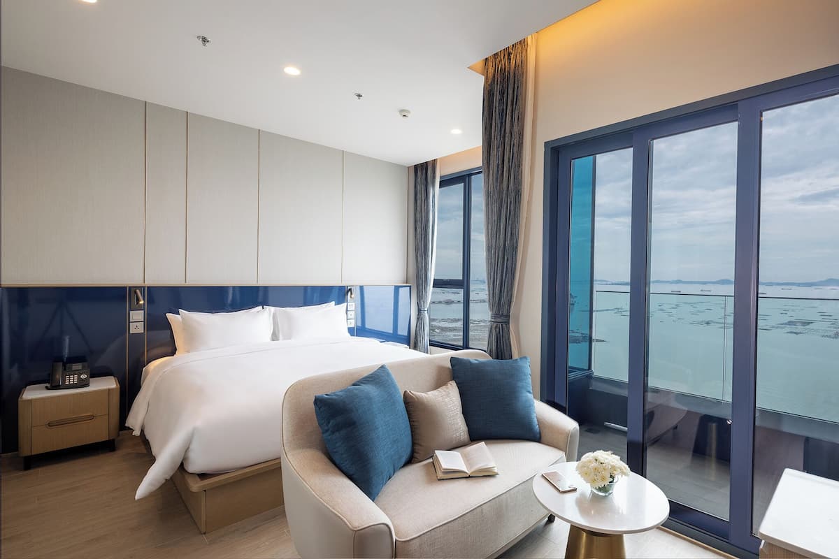 Ein modernes Hotelzimmer mit einem großen Bett, einer Couch, einem kleinen Tisch und Blick aufs Meer.
