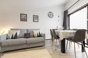 Una sala moderna con un sofá gris, una mesa de comedor con sillas y un amplio ventanal.