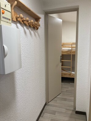 Un pasillo con un estante de madera, una puerta blanca y una cama individual en el fondo.
