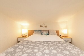 A bedroom with a bed, two bedside lamps, a decorative wall piece, and a patterned bedspread.