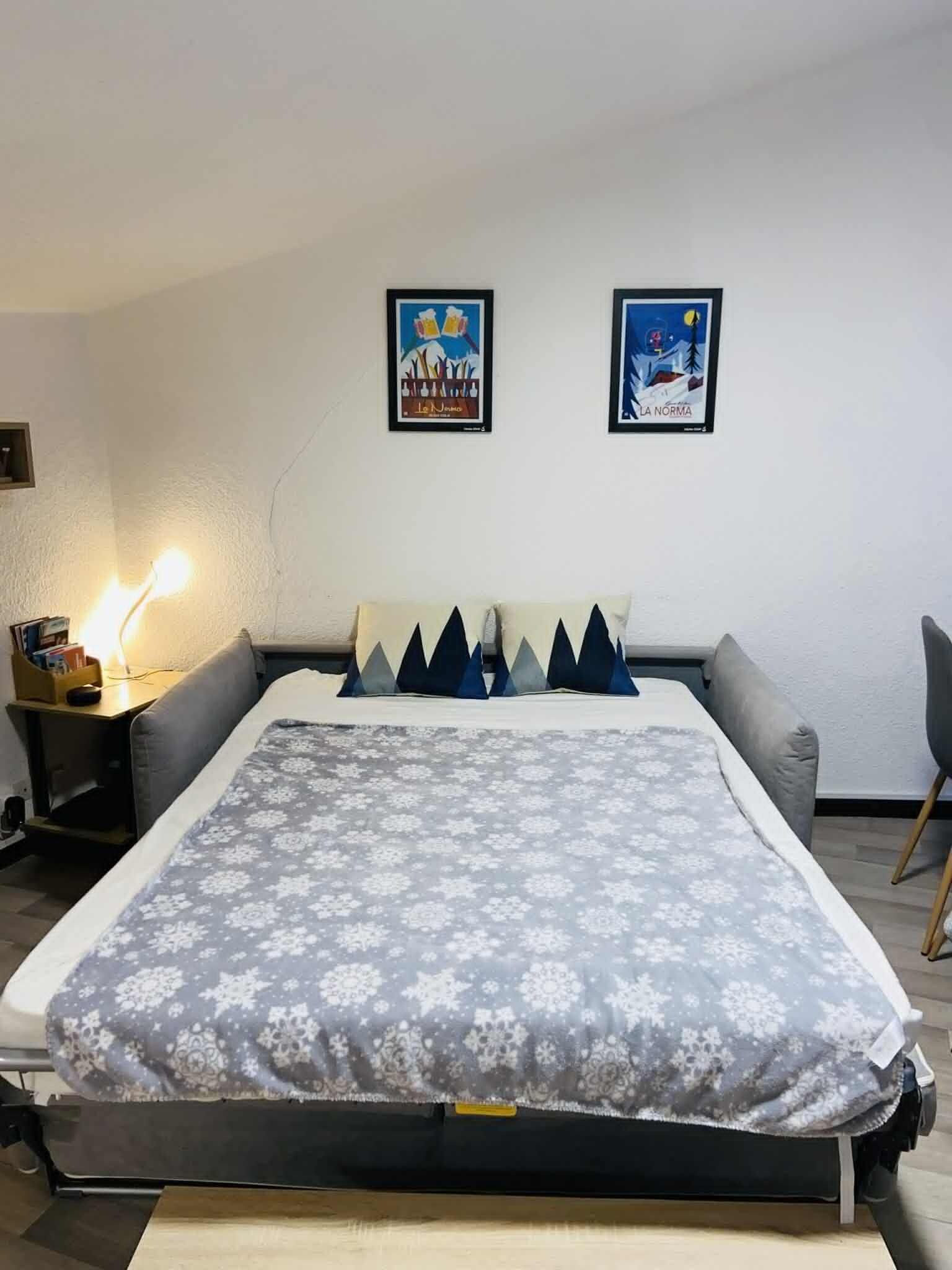 Un dormitorio con cama, mesita de noche, lámpara, dos carteles enmarcados en la pared y una silla.