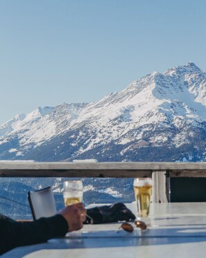Una mesa con dos vasos de cerveza y un par de gafas de sol, con vistas a una montaña nevada.