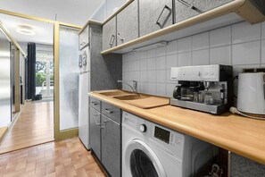 Eine moderne Küche mit grauen Schränken, einer Waschmaschine, einer Kaffeemaschine und einer Holzarbeitsplatte.