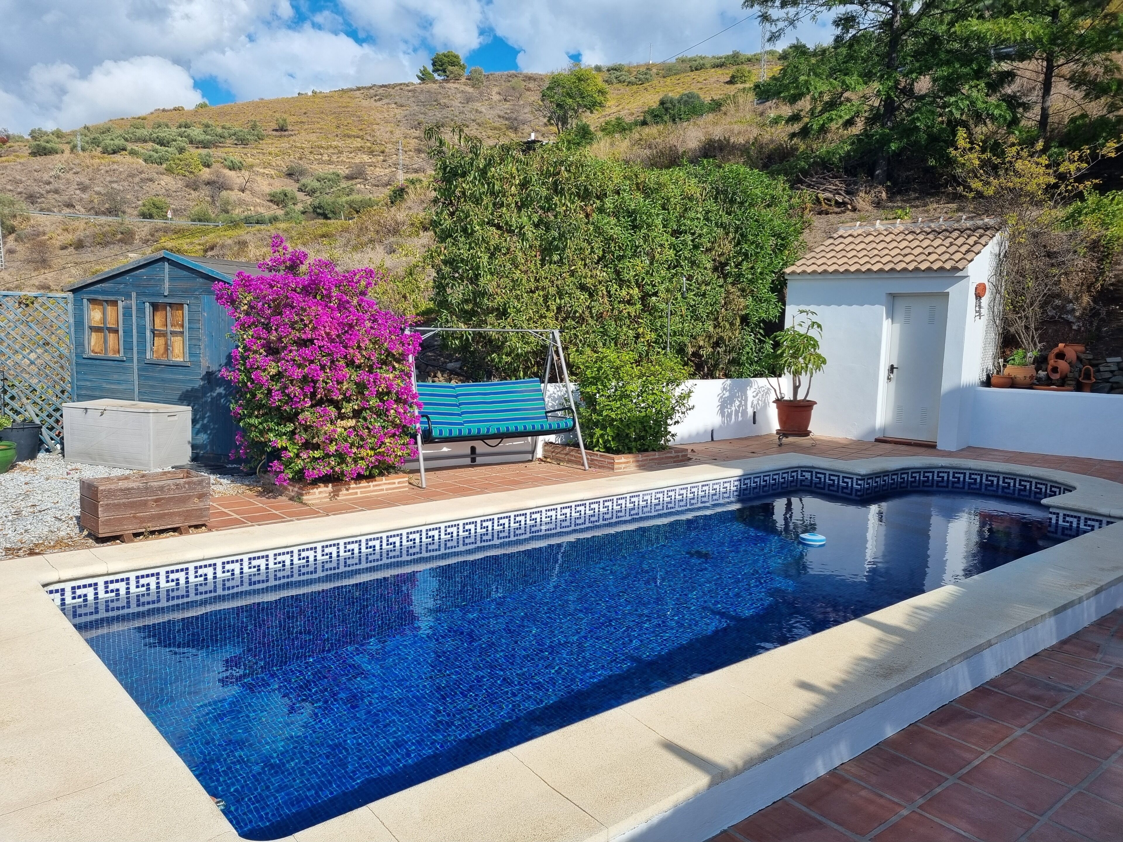 A swimming pool with a geometric tile pattern, surrounded by a patio area with a wooden bench and a swing.