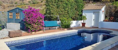 A swimming pool with a geometric tile pattern, surrounded by a patio area with a wooden bench and a swing.