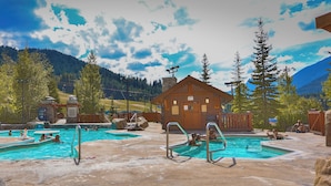 Un espace piscine comprenant plusieurs piscines, des cabanes en bois et un paysage montagneux en toile de fond.