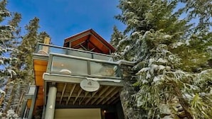Une cabane dotée d’un balcon en verre donnant sur une forêt enneigée.