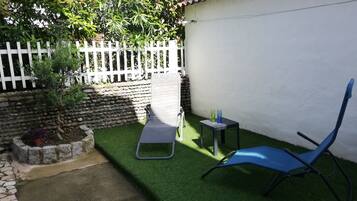 Un pequeño espacio al aire libre con césped artificial, cerca blanca, pared de piedra y una silla azul.