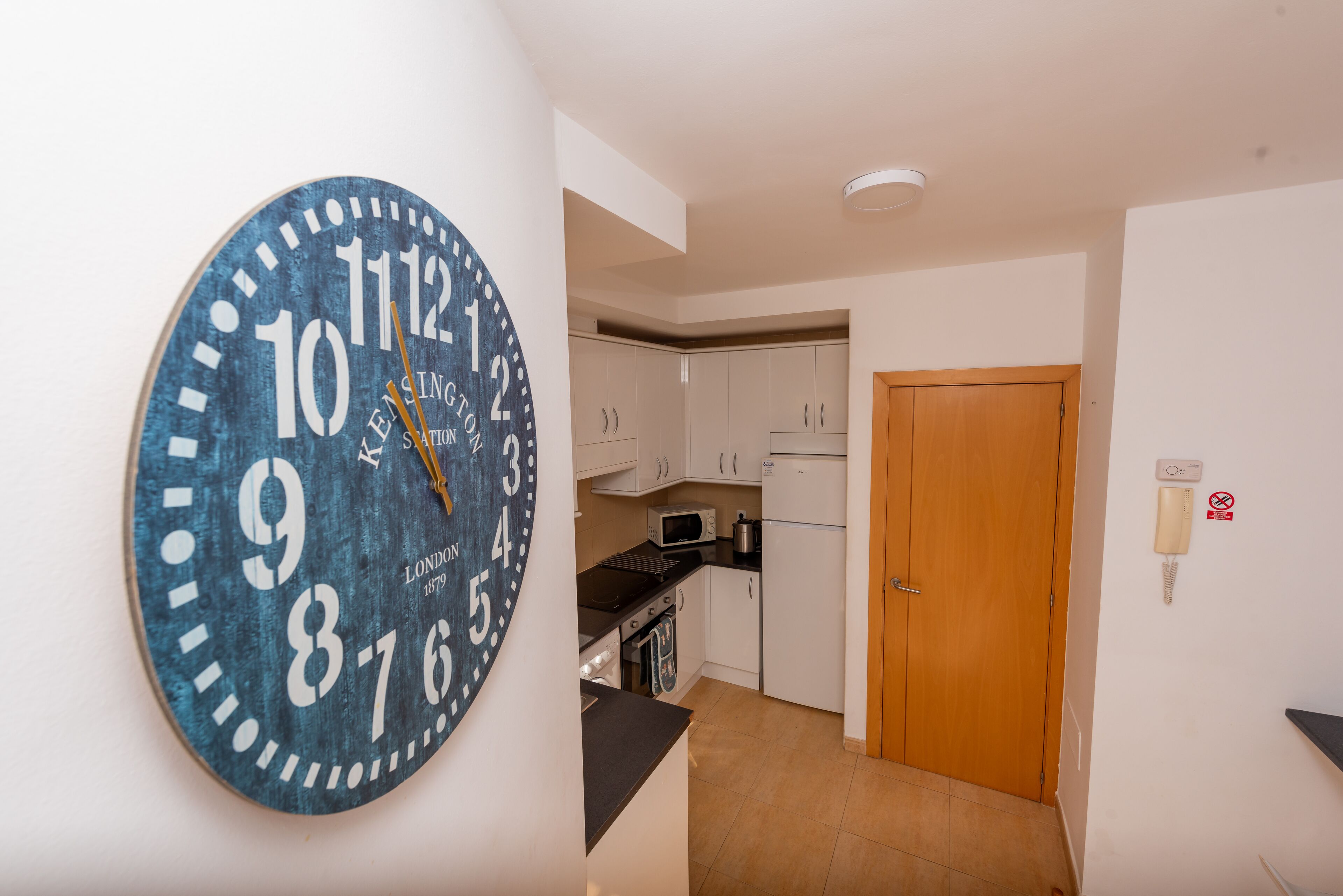 A kitchen with white cabinets, a microwave, a stove, and a clock on the wall.
