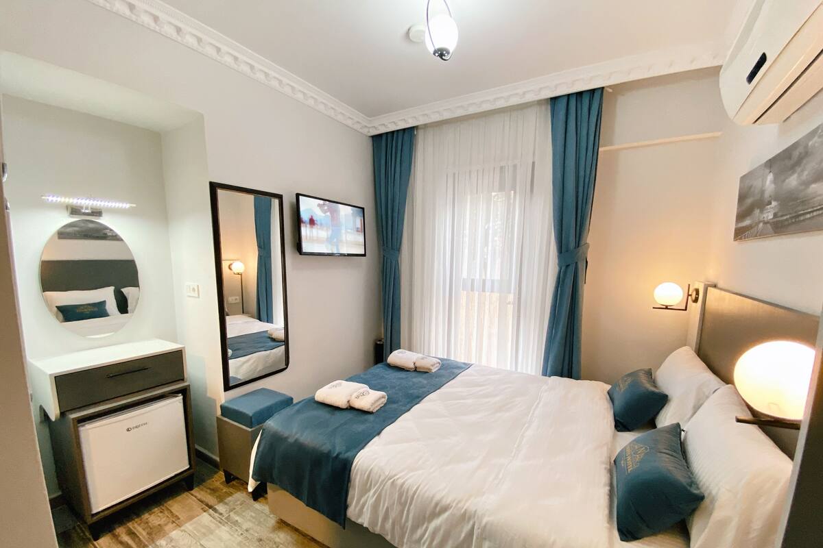 A hotel room with a bed, a bedside table, a mirror, a TV, and a wardrobe.