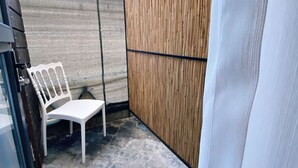 A small outdoor area with a white plastic chair, a bamboo privacy screen, and patterned flooring. - Nefis Hotel City (Fethiye)