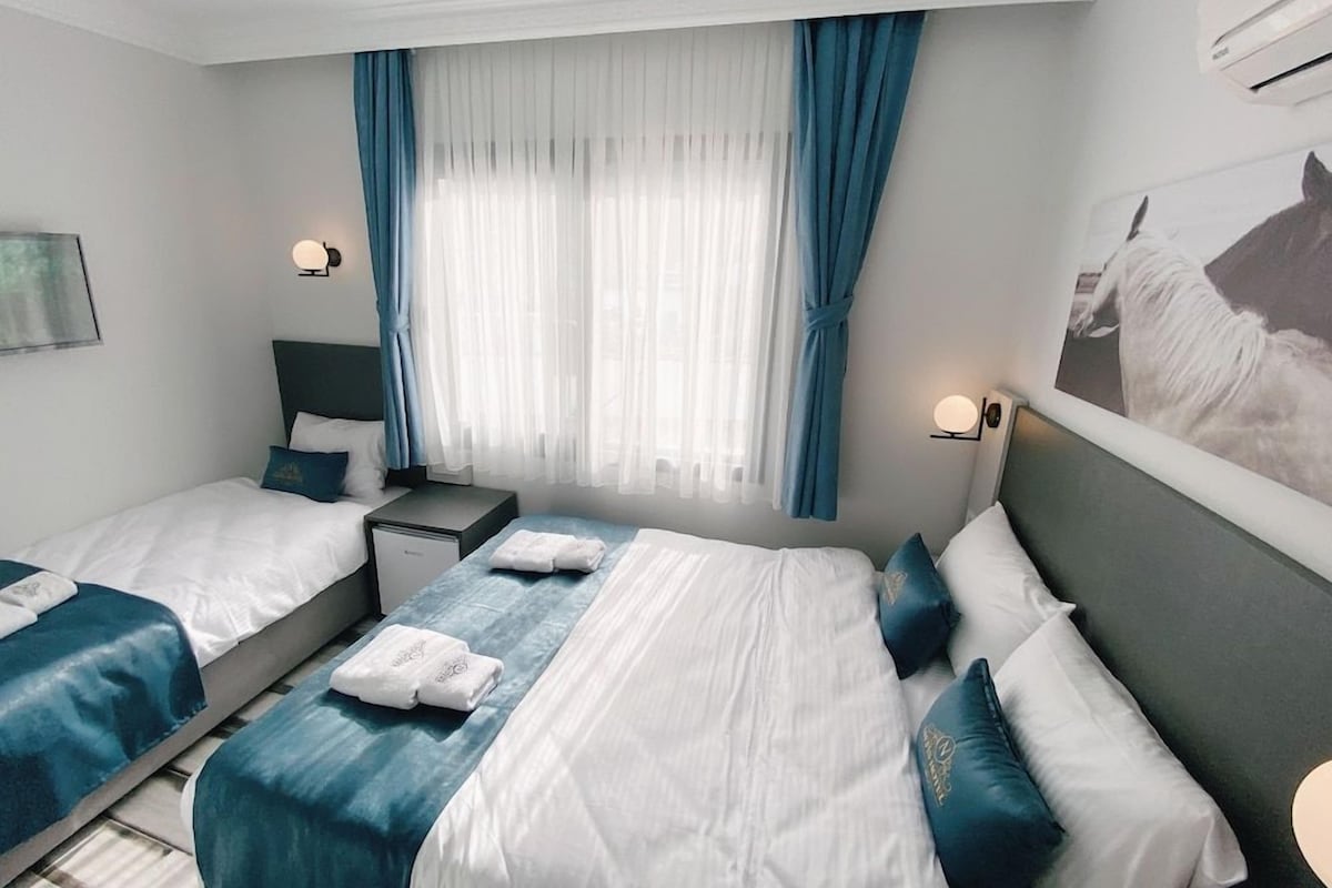 A hotel room with two beds, a nightstand, a wall-mounted air conditioner, and a painting of a horse.