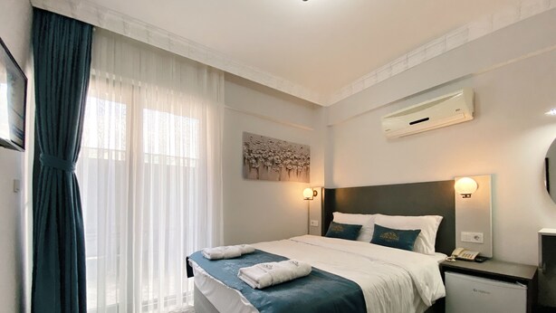 A hotel room with a bed, a nightstand, a wall-mounted air conditioner, and a window with curtains. - Nefis Hotel City (Fethiye)