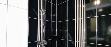 Ducha en esquina con azulejos negros y asiento estampado.