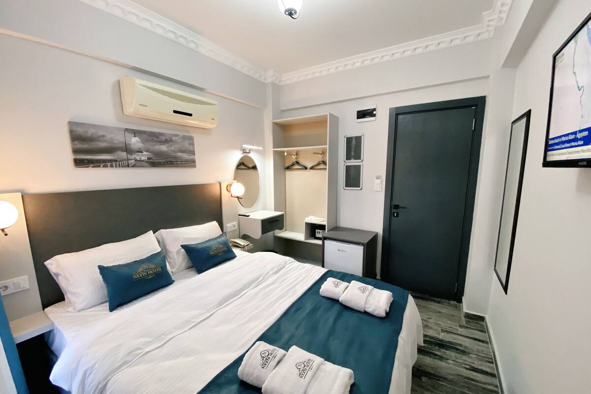 A hotel room with a bed, bedside table, lamp, wardrobe, and a wall-mounted air conditioner.