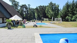Ein Poolbereich mit zwei Pools, Liegestühlen und einem Gebäude mit einem geneigten Dach.