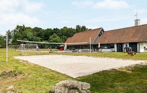 Un terrain de volley-ball avec un filet, un bâtiment doté d’un toit en tuiles et un mât pour drapeau.