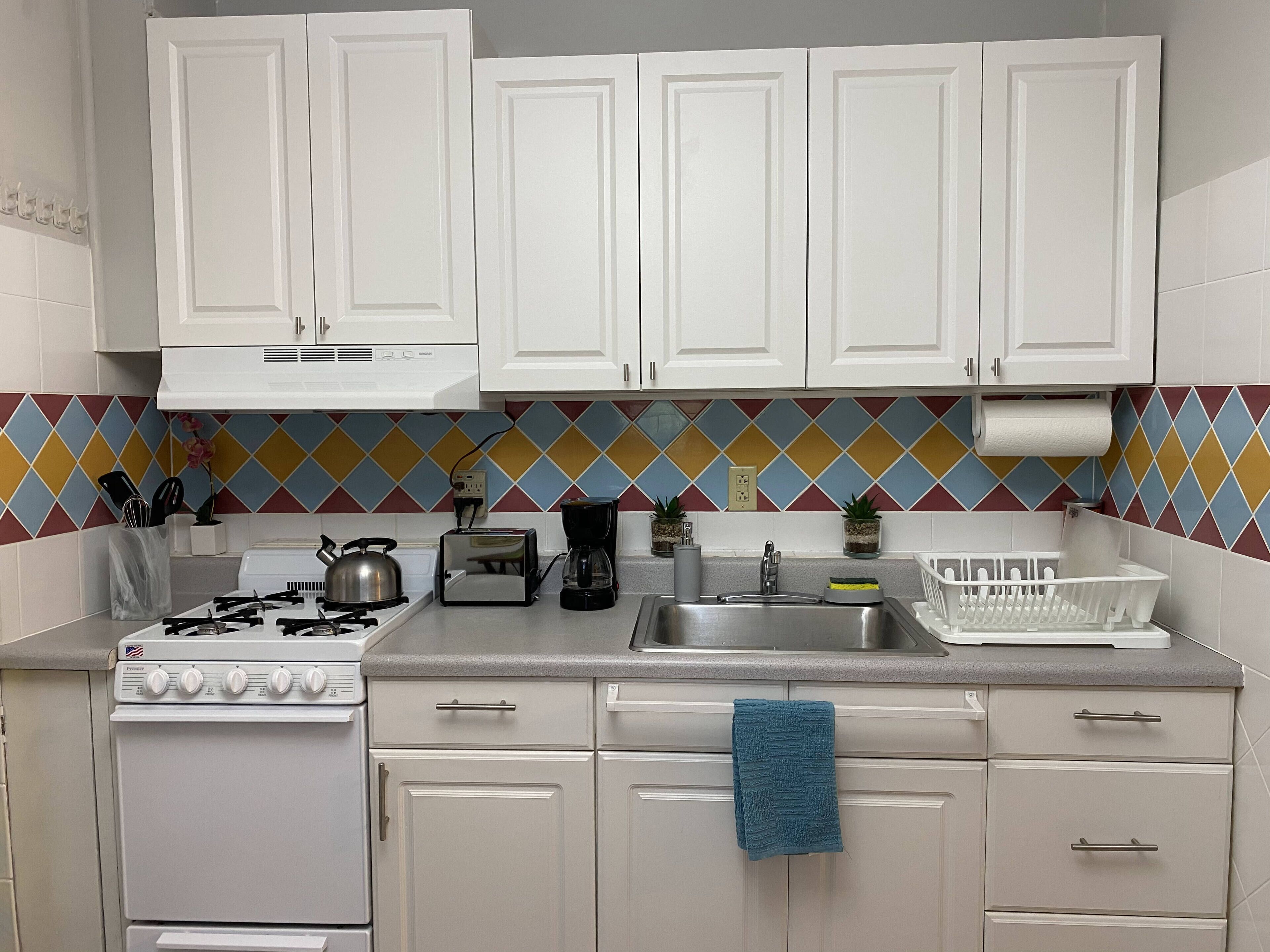 A kitchen with white cabinets, a gas stove, a toaster, a coffee maker, and a sink.