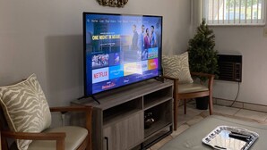 Una sala de estar con televisor mostrando una película, un mueble de madera para entretenimiento, un sofá y un sillón.