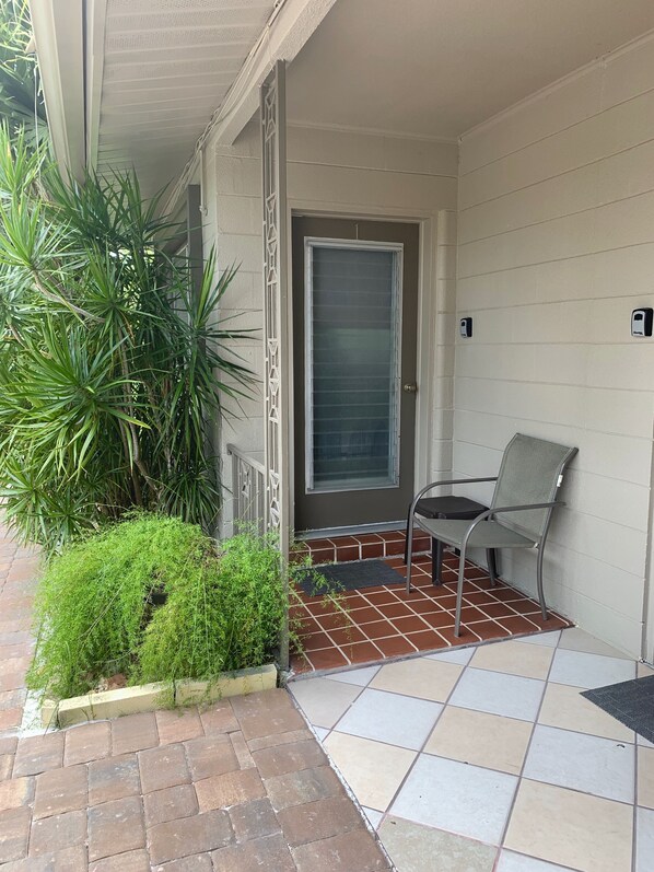 A covered porch with a chair, a door, and potted plants.