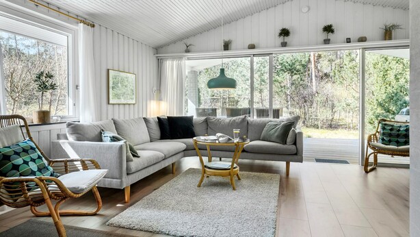 A modern living room with a sectional sofa, wicker chairs, a small round table, and a view of the outdoors through large windows. - Amazing home in Nexø with WiFi (Nexø)