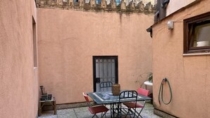 A small outdoor patio with a table and chairs, a potted plant, and a window with a curtain. - Ca' Frutariol Apartment (Venezia)