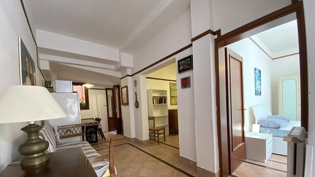 A spacious living area with a dining table, sofa, and a view into another room with a bed and a window. - Ca' Frutariol Apartment (Venezia)