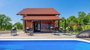 A poolside area with a covered seating area, a pool, and a building with a red-tiled roof. - Amazing home in Perusic with sauna (Perusic)