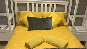 Een bed met een wit frame, gele beddengoed en een grijze deken.