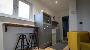 Een moderne keuken met een grijs kastje, een kleine barstoel en een gele bank.
